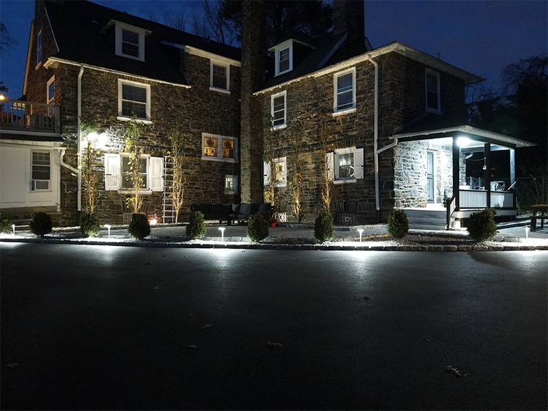 Italian-inspired patio and surrounding plantings illuminated with integrated landscape lighting in Overbrook Farms at night.