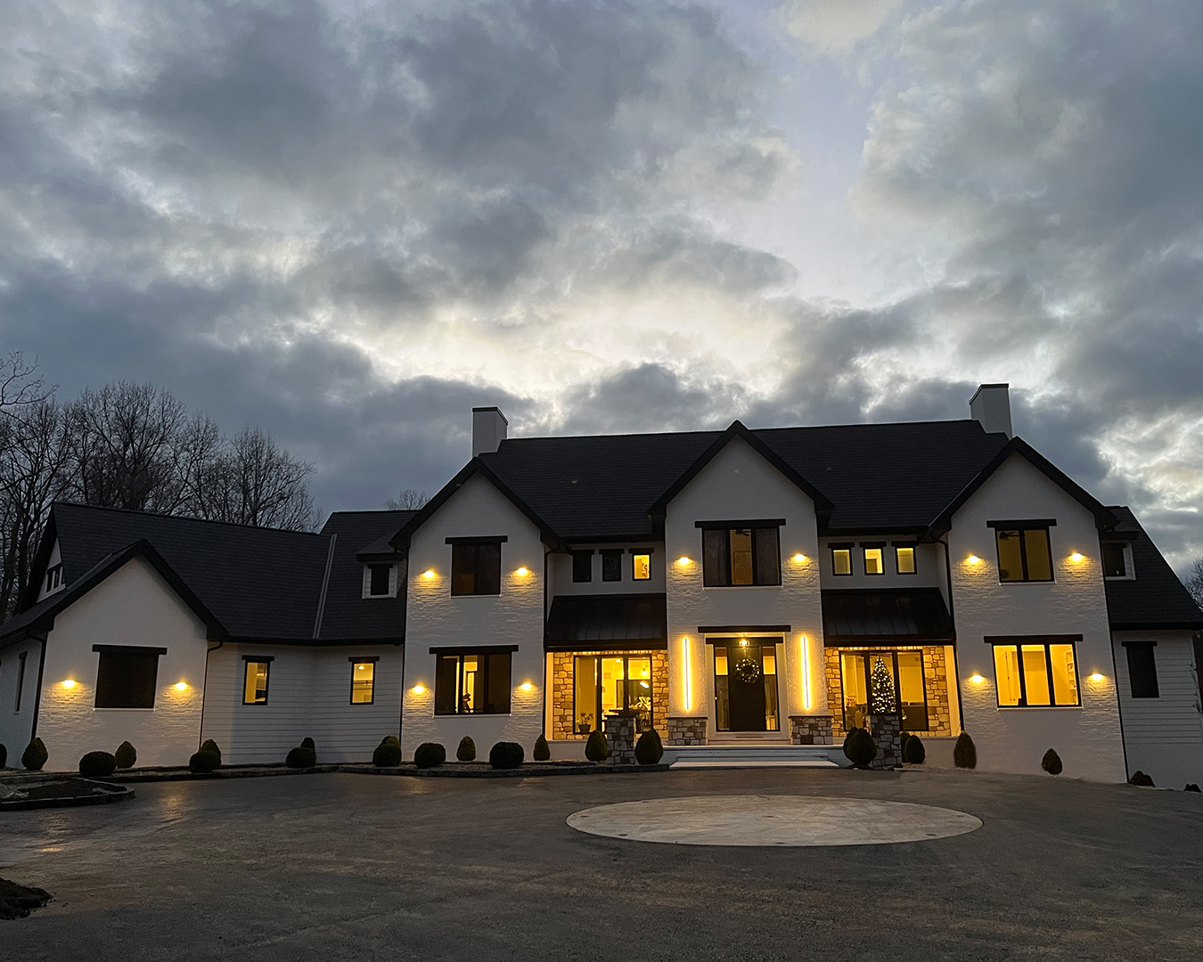 Dusk view of modern farmhouse landscape in Christiana, Pennsylvania, with front yard illuminated by landscape lighting highlighting driveway, plantings, and architectural features