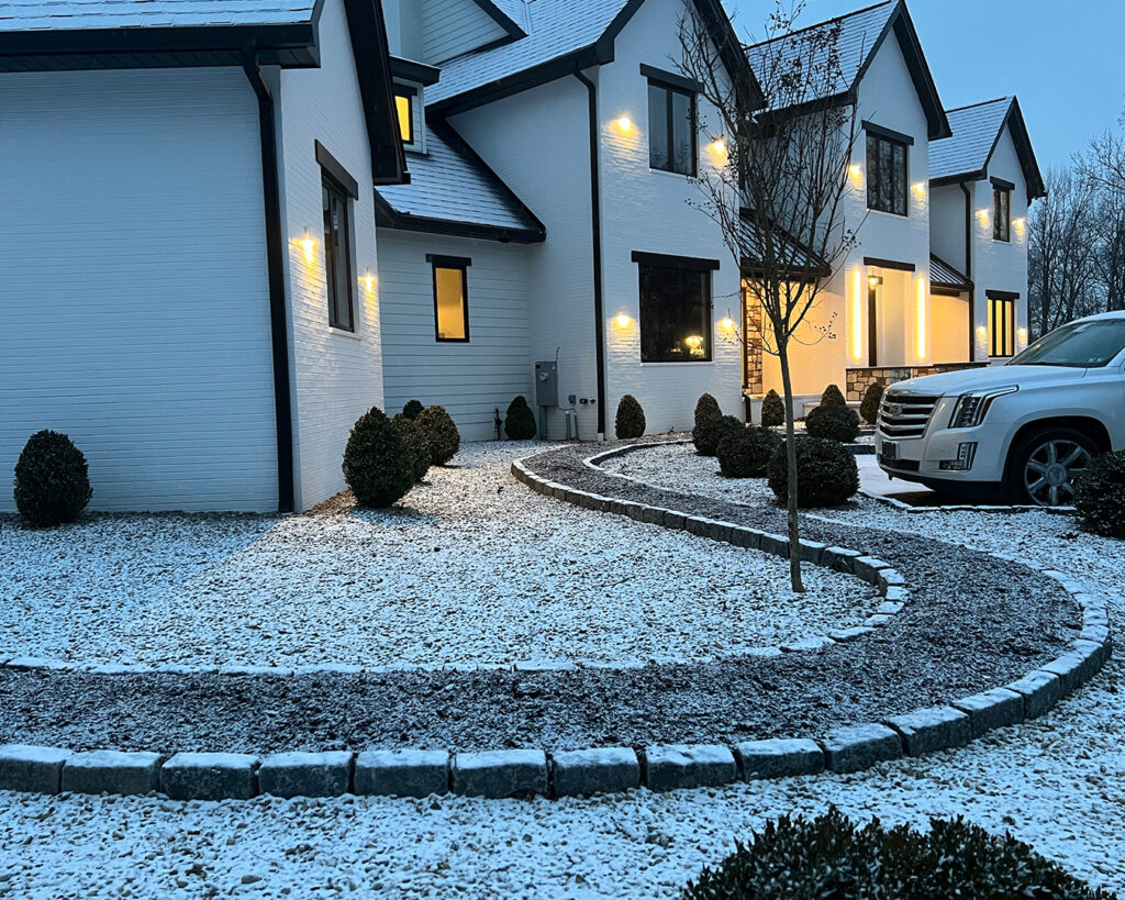 Close-up of cobblestone driveway with light snow and modern farmhouse illuminated in the background in Christiana, Pennsylvania